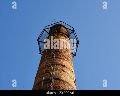 Torre industriale o tubo con balcone di osservazione. Cisterne per fumatori con scala o scale. Camini in mattoni alti sopra l'edificio abbandonato della caldaia per lo sfiato Foto Stock