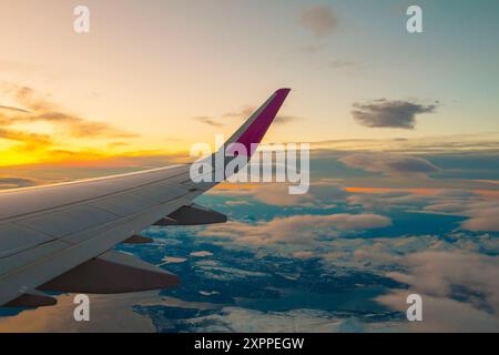 La vista dalla finestra dell'aereo alle nuvole e al tramonto. Ala dell'aeroplano sopra spesse nuvole rosa e arancione. Splendida vista mozzafiato. Foto Stock