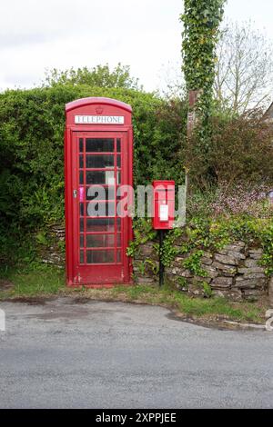 Un vecchio telefono pubblico britannico rosso e una cassetta delle lettere montata su palo alla periferia di un villaggio in Cornovaglia, Inghilterra Foto Stock