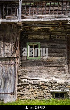 Casa di legno molto vecchia. Piccola finestra in un muro di legno. Elementi di una vecchia casa in legno. Foto Stock