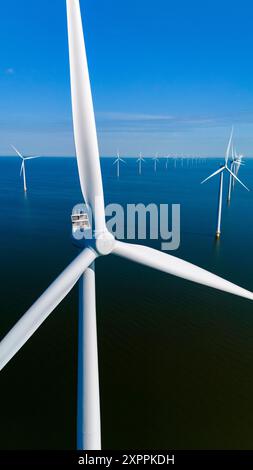 Le pale giganti delle turbine eoliche girano con grazia, sfruttando l'energia eolica nella vasta distesa blu della costa olandese. vista dall'alto di un parco con mulini a vento nell'oceano Foto Stock