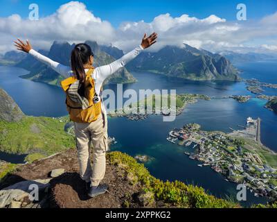Un escursionista si erge trionfalmente in cima a una montagna, braccia allungate, abbracciando l'alba mozzafiato sulle splendide isole Lofoten in Norvegia. Foto Stock