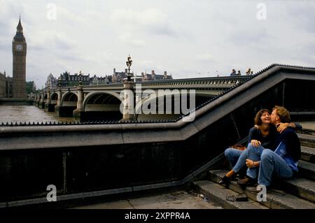 Amanti dell'ora di pranzo, due giovani uffici che flirtano tra loro durante l'ora di pranzo seduti sui gradini sul lato sud del Tamigi e che guardano verso la camera del Parlamento. Londra Inghilterra giugno 1992 1990 Regno Unito HOMER SYKES Foto Stock