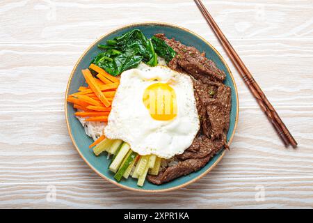 Bibimbap tradizionale coreano con uovo fritto in cima, vista dall'alto su sfondo bianco in legno Foto Stock