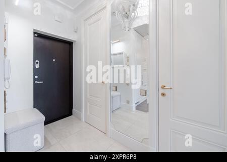 Hall d'ingresso principale. Interno. Porta nera in legno, pavimento marrone. Minimalismo. Luce LED. Porte chiuse per il soggiorno. Panca bianca Foto Stock