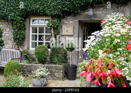 Grassington Yorkshire Regno Unito - 27 luglio 2024. Elegante bed and breakfast esterno con vegetazione lussureggiante, fiori colorati e un'accogliente panca in legno. Foto Stock