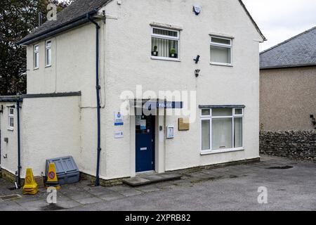 Grassington Yorkshire Regno Unito - 27 luglio 2024. Piccola stazione di polizia rurale con pareti beige, porta blu e due coni stradali gialli in una giornata nuvolosa. Foto Stock