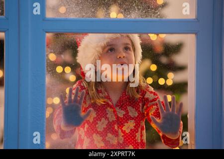 Ragazza giovane guardando fuori della finestra in attesa di Santa per arrivare Foto Stock