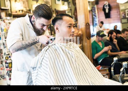 Rotterdam, Paesi Bassi. Negozio del barbiere Schorem. Barbiere aiutando il suo cliente nel suo negozio di barbiere mediante il taglio e la modellazione dei suoi capelli. Foto Stock