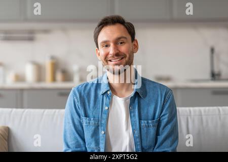 Uomo sorridente che indossa una camicia in denim seduto sul divano in cucina Foto Stock
