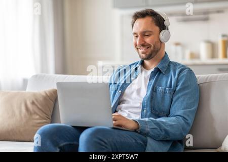 Uomo che lavora su un laptop in salotto mentre indossa le cuffie Foto Stock