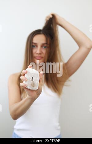 Problema di perdita dei capelli. La giovane donna preoccupata mostra una spazzola con un mucchio di capelli caduti dopo la pettinatura. Periodo post-partum, disturbi mestruali o endocrini, ho Foto Stock