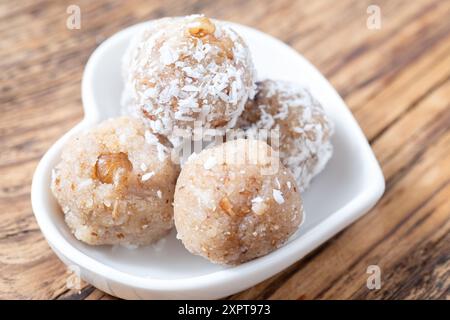 Vista dall'alto di cinque palline di cocco servite in un piatto bianco a forma di cuore su un rustico tavolo di legno. Perfetto per spuntini sani o dessert. Foto Stock