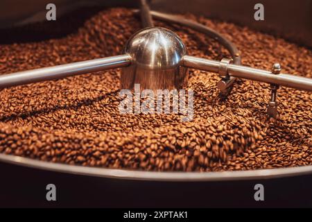 Primo piano dei chicchi di caffè appena tostati che si raffreddano in una grande tostatura industriale, evidenziando il processo di produzione del caffè Foto Stock