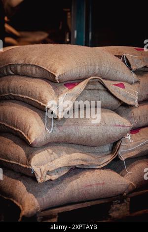 Pile di sacchi di burlap pieni di chicchi di caffè vengono immagazzinati in un magazzino Foto Stock