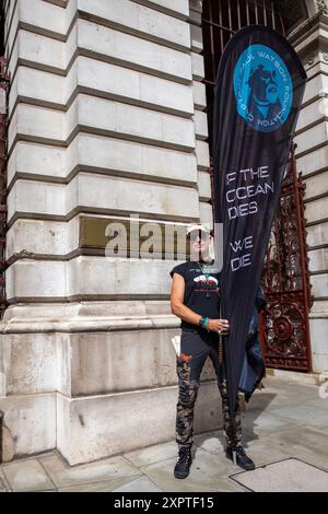 Un manifestante tiene uno striscione davanti al segno del Foreign and Commonwealth Office durante la manifestazione. I sostenitori dell'attivista anti-baleniera Paul Watson tennero una manifestazione fuori dal Foreign and Commonwealth Office a Westminster, nel centro di Londra. Il piccolo gruppo di manifestanti chiede il suo immediato rilascio. Il fondatore e co-fondatore di Greenpeace è stato arrestato in Groenlandia con un mandato di arresto internazionale e ora sta per essere deportato in Giappone. Il settantacinquenne fu accusato di aver violato e aggredito una nave baleniera giapponese nell'Oceano meridionale il 2010 febbraio. E. Foto Stock