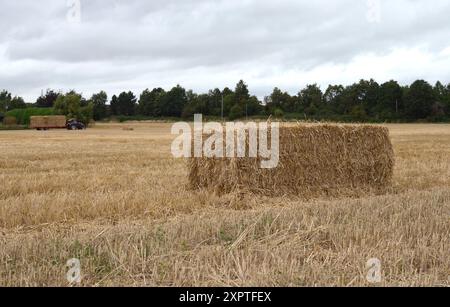 Una fotografia del tempo di raccolta a Stratford upon Avon, Inghilterra, che mostra una balla di paglia e un paesaggio di sfondo con attrezzature agricole. Foto Stock