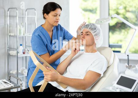 Giovane cosmetologa che esamina il volto di un giovane uomo Foto Stock