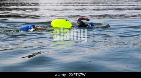 Un primo piano di un nuotatore che nuota in mare aperto indossando un dispositivo galleggiante di sicurezza verde neon nel Long Island Sound. Foto Stock