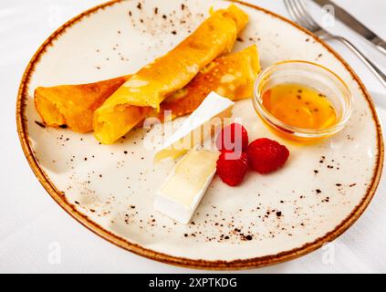 Pancake sottili con fette di brie, lamponi e miele Foto Stock