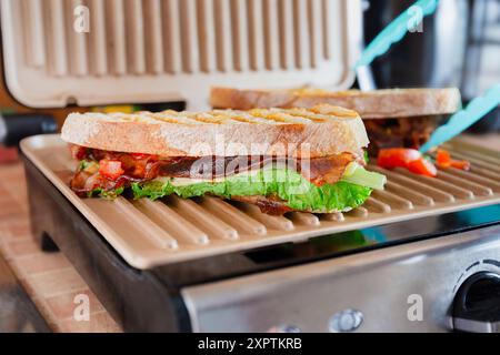 Primo piano di un panino italiano alla griglia con pancetta, lattuga e pomodoro su una pressa per panini, pronto per essere servito. Foto Stock