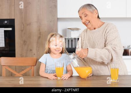 Una bambina carina con la sua nonna che versa succo in cucina Foto Stock