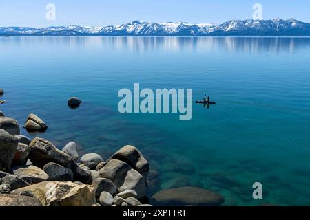 Kayak sul lago Blue Mountain - Una crociera in kayak sulle acque cristalline del lago Tahoe, con cime innevate che torreggiano a riva, CA-NV, Stati Uniti. Foto Stock