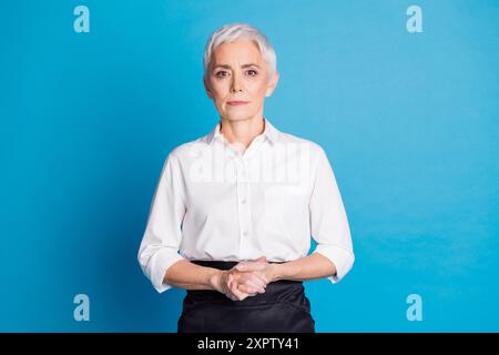 Foto di un'attraente donna anziana pronta a servire il cliente, il proprietario di un piccolo business cafè, vestito da cameriera in uniforme isolata su sfondo di colore blu Foto Stock