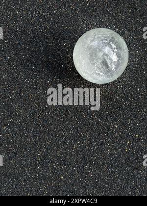 Sfera di cristallo su sfondo di sabbia nera che riflette la luce Foto Stock