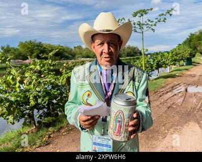 Jhon Smith Noriega posa per un ritratto accanto al canale superiore a Laguna del Nainari nella città di Obregón, Sonora, Messico, il 14 luglio 2024. Jhon indossa un costume del gruppo musicale popolare o regionale la banda chiamato lLaberinto mentre chiede sostegno finanziario con una barca con l'immagine della Vergine di Guadalupe per "mi Casa Albergue" (foto di Luis Gutiérrerez / Norte foto) Jhon Smith Noriega posa para un retrato junto al Canal alto en la Laguna del Nainari en ciudad Obregón Sonora México el 14 julio 2024. Jhon viste de traje de la agrupación de músical Popular o Regional de la banda Foto Stock