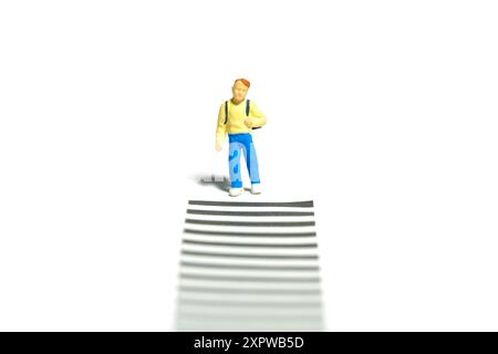 Fotografia di piccoli personaggi in miniatura. Un ragazzo studente che aspetta il valico di zebra sideroad. Isolato su sfondo bianco. Foto immagine Foto Stock