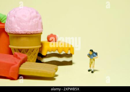 Fotografia di figure giocattolo per persone in miniatura. Concetto di cibo sano e pausa pranzo. Un ragazzo studente dell'asilo in piedi accanto a snack e torta. Isolato Foto Stock