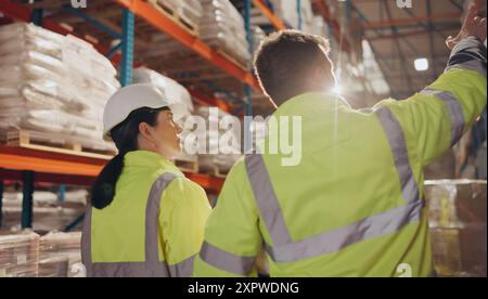 Logistica, colleghi e camminate in fabbrica, colloqui e inventario delle scorte per la spedizione e l'ispettore. Comunicazione, casco e persone in magazzino Foto Stock