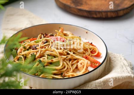 Pasta fritta in padella con gamberi, broccoli, funghi e pomodoro. Servita su un piatto bianco. Foto Stock