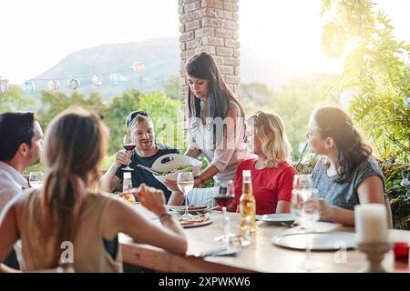 Tavolo, cena e persone con cibo per patio per nutrizione, conversazione e mangiare insieme. All'aperto, amici e discussione con bevande in cortile per Foto Stock