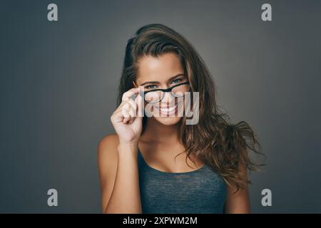 Donna, ritratto e felice con gli occhiali in studio su sfondo grigio per prescrizione, occhiali e vista. Persona femminile, sorriso e soddisfatto o. Foto Stock