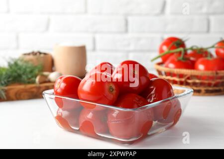 Gustosi pomodori sottaceto nel recipiente su un tavolo bianco Foto Stock