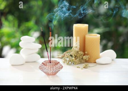 Bastoncini di incenso che si mescolano nel supporto vicino a pietre, candele e fiori secchi su un tavolo di legno all'aperto Foto Stock