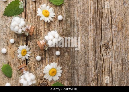 Rimedio omeopatico. Composizione piatta con molte pillole, bottiglie e fiori di camomilla su un tavolo di legno, spazio per il testo Foto Stock