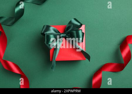 Bellissima confezione regalo rossa con fiocco luminoso e nastri su sfondo verde, piatto Foto Stock