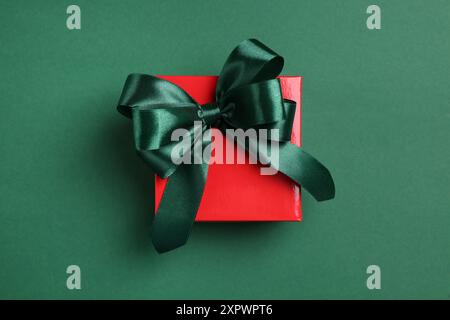 Bellissima confezione regalo rossa con fiocco luminoso su sfondo verde, vista dall'alto Foto Stock