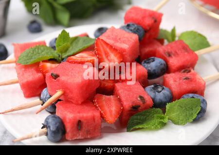 Spiedini con gustosi anguria, fragole, mirtilli e menta sul tavolo, primo piano Foto Stock