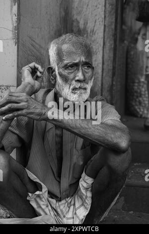 Vecchio vecchio vecchio vecchio povero indiano non identificato con un viso rugoso marrone scuro e capelli grigi e una barba sembra seria. Anziano senzatetto indiano seduto o Foto Stock