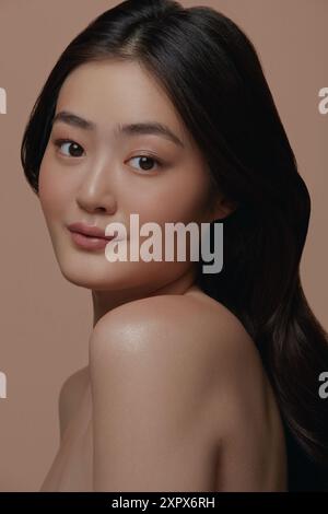 Foto in studio di una bella giovane donna asiatica con una pelle fresca e pulita su sfondo beige. Foto Stock