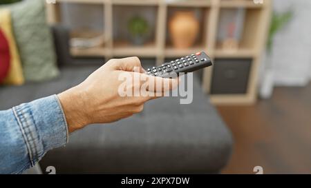 Primo piano di un uomo che tiene in mano un telecomando in un moderno salotto. Foto Stock