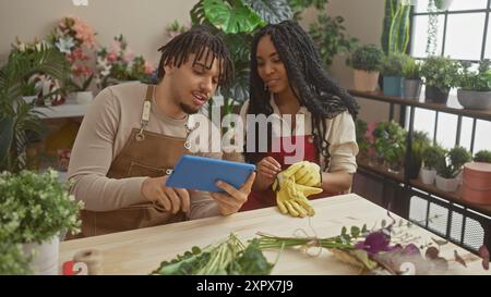 Fioristi uomo e donna in grembiuli con tablet in un negozio di fiori pieno di piante Foto Stock