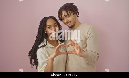 L'uomo e la donna affettuosi insieme creano la forma del cuore con le mani contro il muro rosa Foto Stock