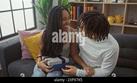 Una coppia felice d'amore condivide un regalo in casa, con l'uomo e la donna che si godono un momento insieme nel loro salotto di appartamento. Foto Stock