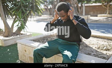 Il giovane afroamericano che indossa le cuffie si trova in un parco cittadino. Foto Stock