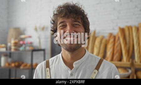 Bel giovane sorridente in una panetteria, con vari tipi di pane e pasticcini esposti sullo sfondo Foto Stock